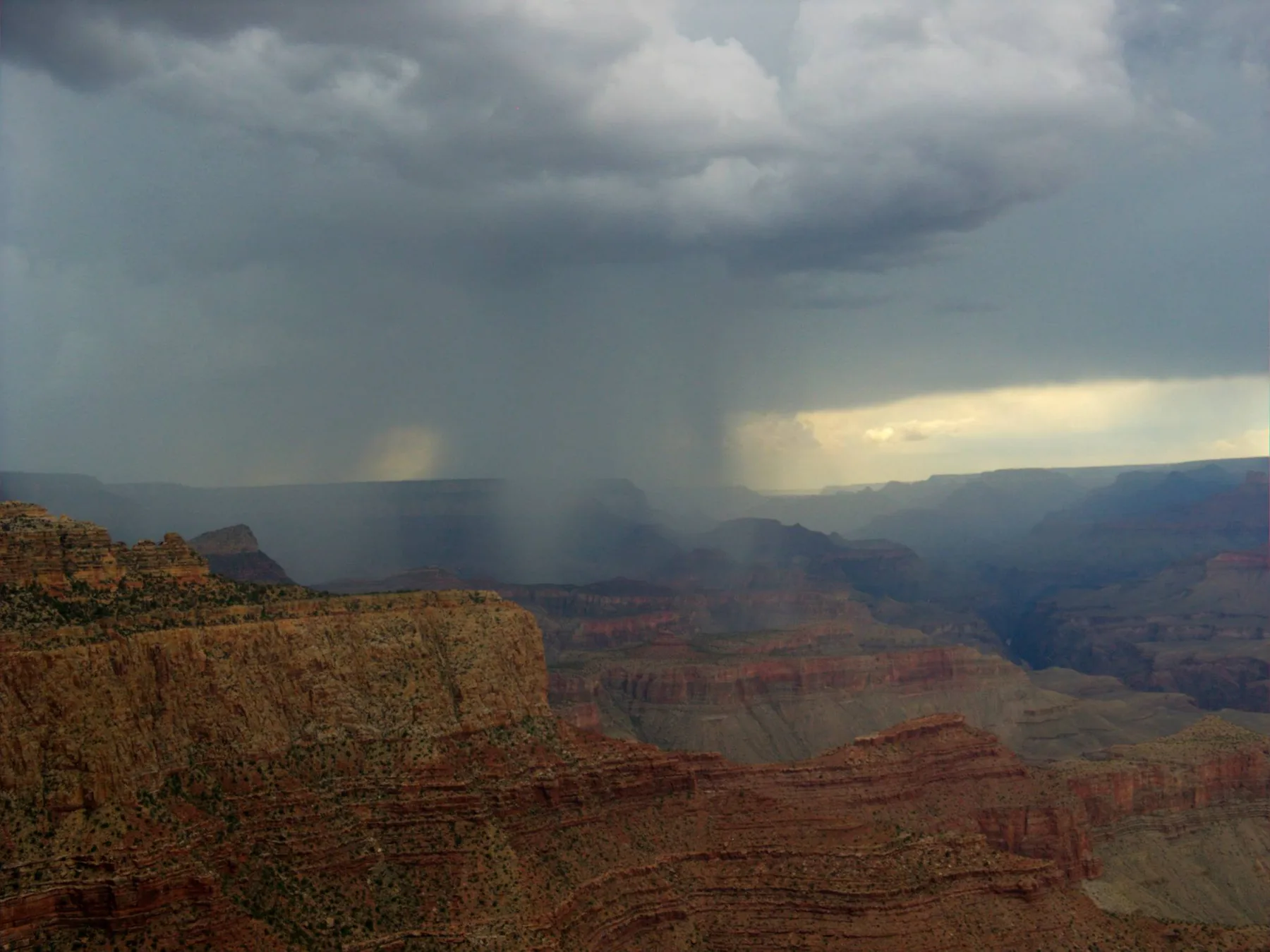 Sunlight breaking through storm clouds over layered red-rock canyon walls